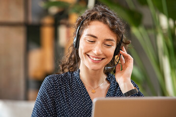 Smiling woman talking to customer on headphones - obrazy, fototapety, plakaty