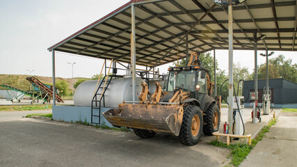 Yellow tractor on gas station. Refill. Heavy equipment. Tanks with fuel.