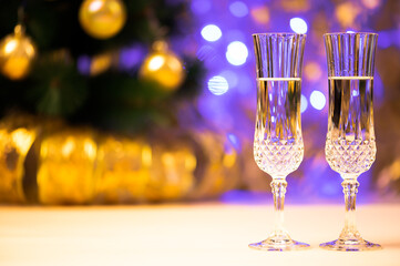 two crystal glasses on the table, against the background of a Christmas tree with toys and a Christmas garland burning with blue lights