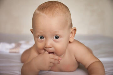 A charming boy licks his fingers while lying on his stomach. The view of a serious person