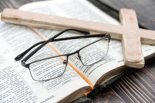 A large wooden cross and glasses lie on the bible, close-up.