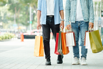 Cropped image of young men walking down the street with many shopping bags in hands