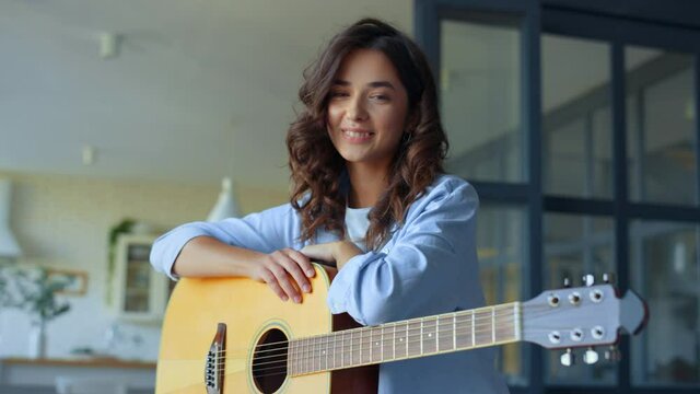 Dreamy girl holding acoustic guitar at home. Happy woman looking at camera