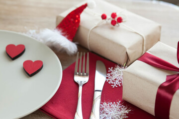 Festive table setting for Valentine's Day with plate, gift boxes, fork, knife and hearts on a wooden table. 
