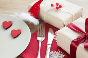 Festive table setting for Valentine's Day with plate, gift boxes, fork, knife and hearts on a wooden table. 