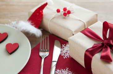 Festive table setting for Valentine's Day with plate, gift boxes, fork, knife and hearts on a wooden table. 