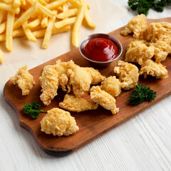 Homemade Popcorn Chicken on a rustic wooden board on a white wooden background, side view. Close-up.