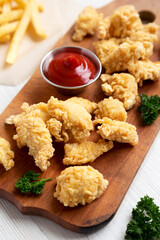 Homemade Popcorn Chicken on a rustic wooden board on a white wooden surface, low angle view.