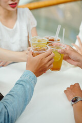 Close-up image of young people toasting with plastic glasses of iced tea