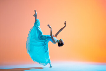 Ballerina in a light blue dress is dancing on colored backlit background
