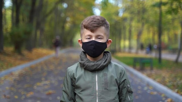 Boy child  wearing face mask outside in the Coronavirus COVID-19 pandemic. standing outside, wearing a black mask, protecting his face from polluted airborne dust and wearing a mask to protect 