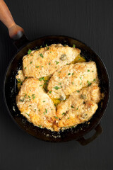 Homemade Italian Chicken Piccata in a cast-iron pan on a black background, top view. Flat lay, overhead, from above.