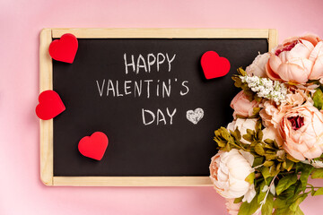 A black slate with the words "Happy Valentine's day" on it. Romantic pink background with flowers and hearts