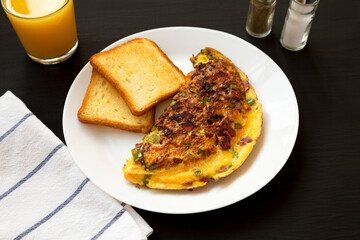 Homemade Denver Omelette on a white plate on a black surface, low angle view.