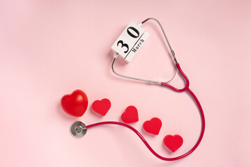 The concept of celebrating Doctor's Day with a stethoscope and a heart on a pink background. Wooden calendar with the date March 30