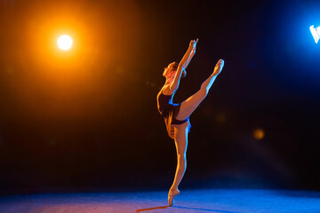 Ballerina in a black dress is dancing on black background illuminated by multicolored beams of...