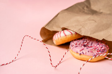 Donuts protrude from an eco-friendly paper bag on a pink background