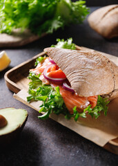 .Healthy sandwich with rye bread bun, salmon, avocado, onion and salad served on a wooden rustic board.