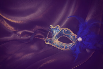 Photo of elegant and delicate gold Venetian mask over dark silk background. vintage filtered