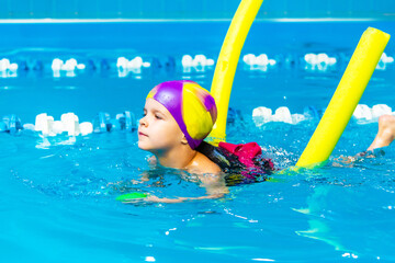 A little boy with a life jacket on his chest learns to swim in an indoor pool.