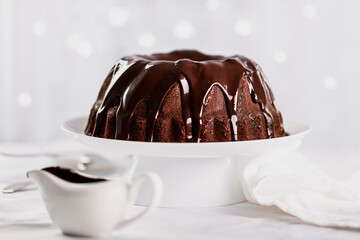 Dark chocolate cake covered with icing on a white stand. Selective focus.