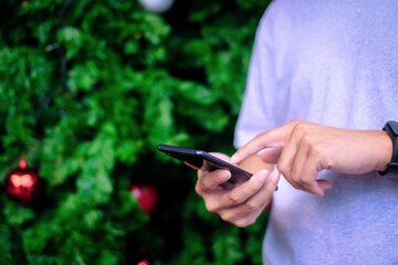 Man holding blank white screen smartphone with christmas tree background, Technology concept.
