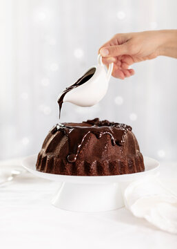 Dark chocolate cake covered with icing on a white stand. Selective focus.