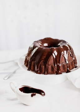 Dark chocolate cake covered with icing on a white stand. Selective focus.