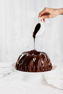 Dark chocolate cake covered with icing on a white stand. Selective focus.