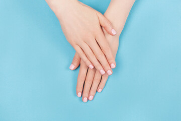 Manicure and nail care concept. Two woman hands with perfect pastel pink nail polish on aqua blue background. Summer minimal manicure. Flat lay, top view. Copy space.