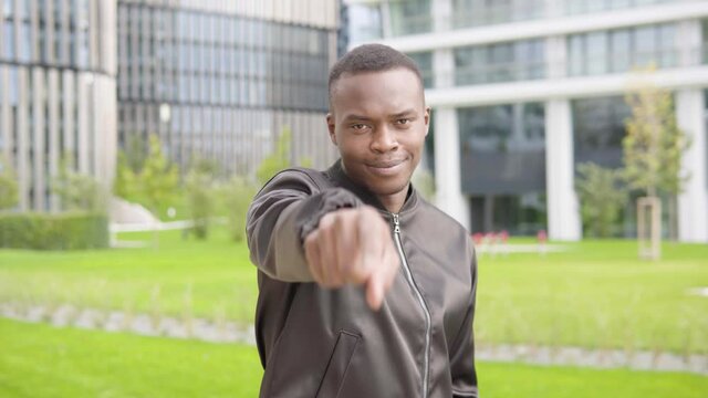 A young black man points at the camera and nods - office buildings in the blurry background