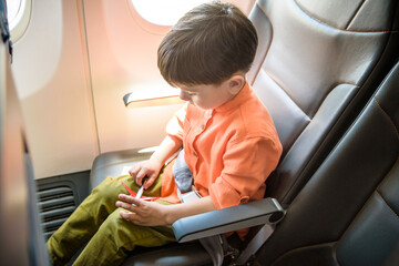Child in airplane. Kid in air plane sitting in window seat. Flight entertainment for kids. Traveling with young children. Kids fly and travel. Family summer vacation. Little boy with toy in airplane