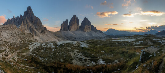 Golden hour over famous Tre Cime di Lavaredo (Drei Zinnen), mountains in Italian Dolomites. The mountains are surrounded with orange and pink clouds. Desolated and raw landscape. Sunset time. Serenity