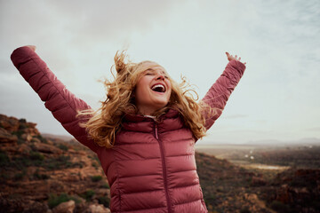 Cheerful young woman with hands raised and outstretched mountaineer with hair flying in wind...