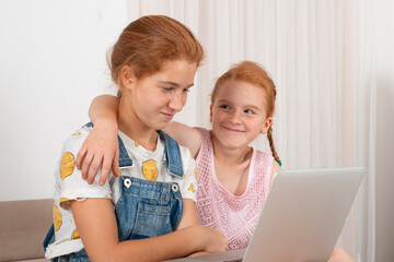 Two young attractive girls teenager with red hair  lies on a sofa at home using laptop.