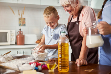 Joyous senior woman happily cooking happily with two grandkids