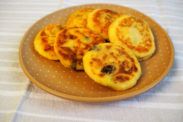 six yellow sugar-free cheesecakes with banana and raisins in corn flour lie in a brown polka-dot round plate on a light white and gray striped tablecloth side view . cooking cheesecakes at home