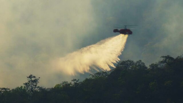 Fire fighting helicopter dropping water on forest fire