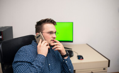 Young caucasian businessman in blue shirt is talking on phone with someone. Businessman is trying to help someone to solve the problem.