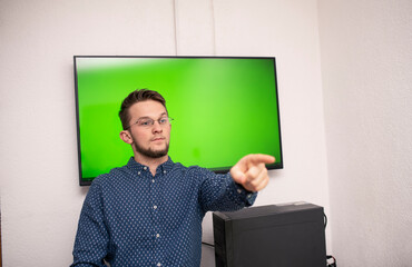 young caucasian businessman wearing glasses points a finger at someone in front of a smart board with a green screen