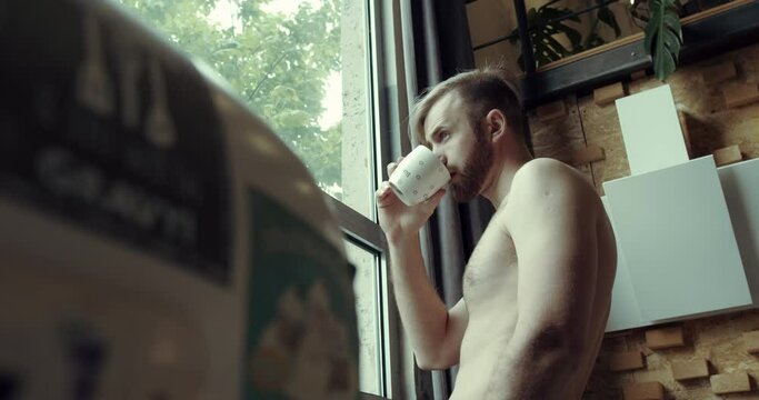 a young man with a naked body serves a morning coffee in the kitchen at home.