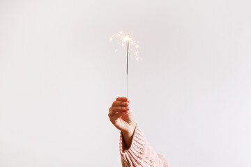 Cropped shot of young woman's hand holding the burning sparkler isolated on white background. Close...