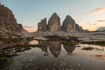 Fototapeta na wymiar Golden hour over the Tre Cime di Lavaredo (Drei Zinnen), mountains in Italian Dolomites. The peaks reflect in a paddle. The mountains are surrounded with orange and pink clouds. Sunset time. Serenity