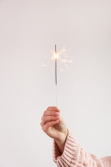 Cropped shot of young woman's hand holding the burning sparkler isolated on white background. Close up, copy space for text. New year and christmas themed backdrop.
