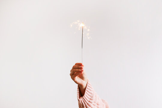 Cropped shot of young woman's hand holding the burning sparkler isolated on white background. Close up, copy space for text. New year and christmas themed backdrop.