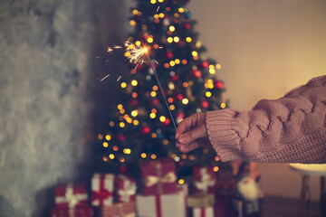 Cropped shot of young woman wearing pink knitted sweater holding the burning sparkler, over the...