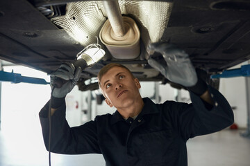 Young caucasian man checking bottom of auto on lift
