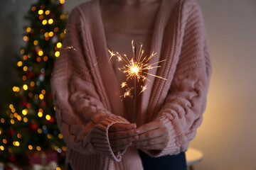 Cropped shot of young woman wearing pink knitted sweater holding the burning sparkler, over the...