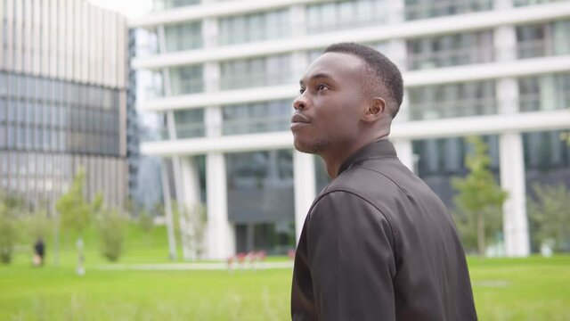 A young black man looks around - office buildings in the blurry background