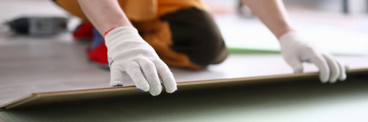 Close-up of adult man installing new laminated wooden floor in room. Professional worker in protective white gloves. Qualified foreman. Construction site concept